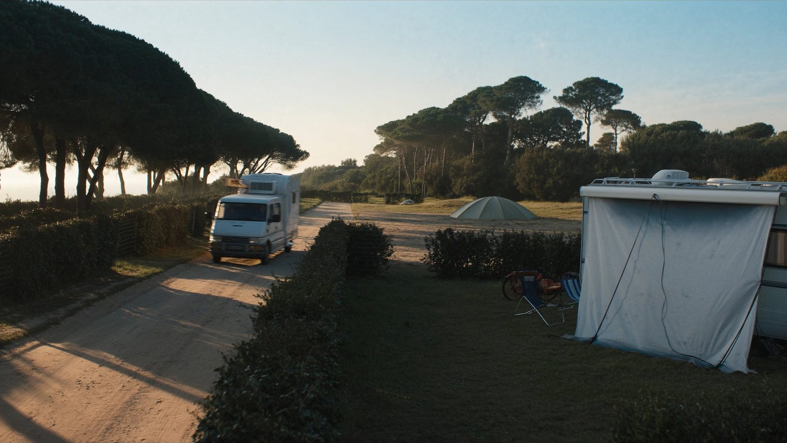 Camper che arriva sul viale del campeggio la mattina presto, accanto a una piazzola in partenza
